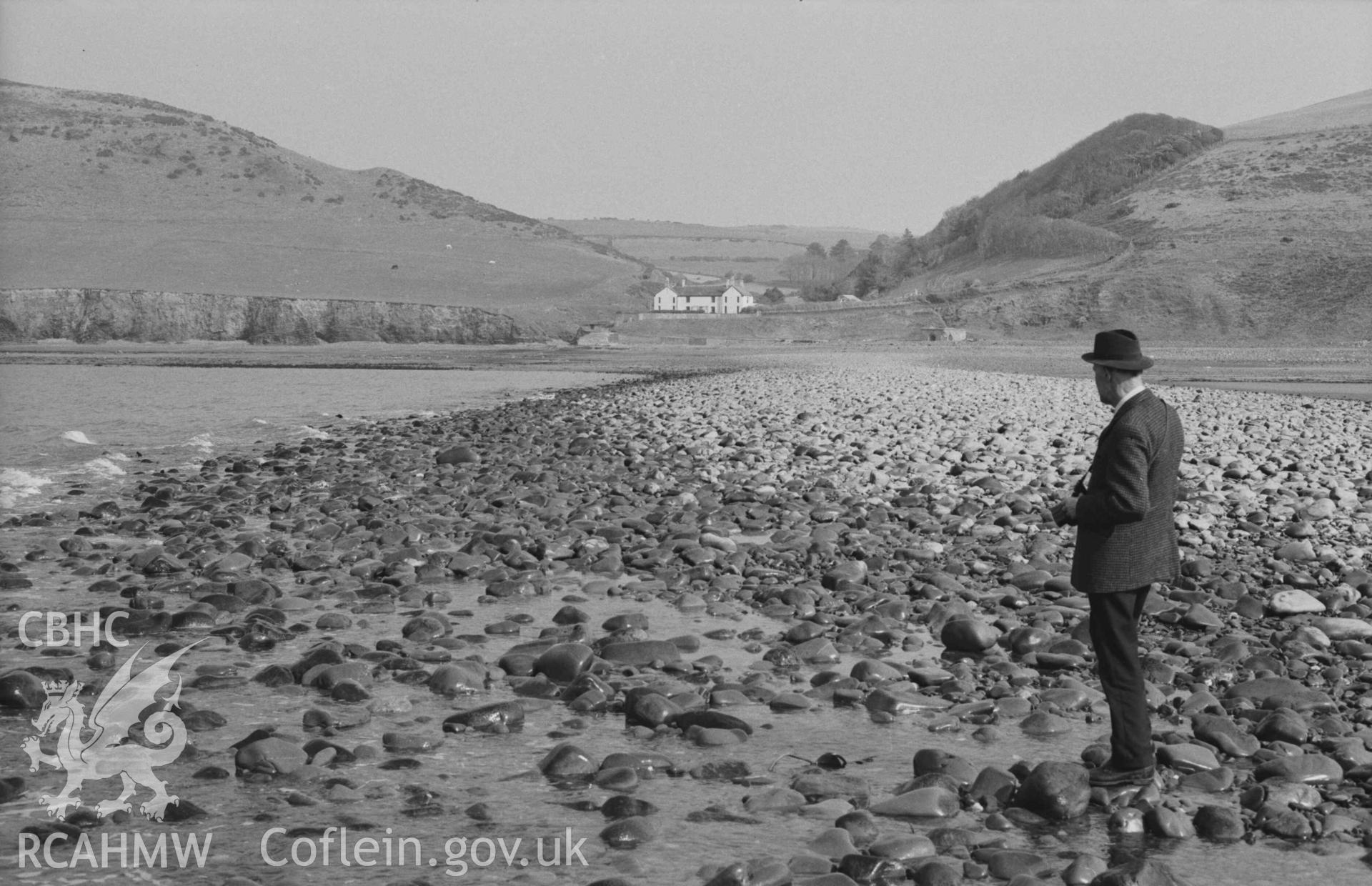 Digital copy of a black and white negative showing view to Wallog house from the extreme tip of Sarn Cynfelyn at lowest ebb of 29ft 7inch tide; 15:45-15:55hrs, Figure with camera in foreground. Photographed by Arthur Chater on 4 April 1969. Looking east from Grid Reference c. SN 584 858.