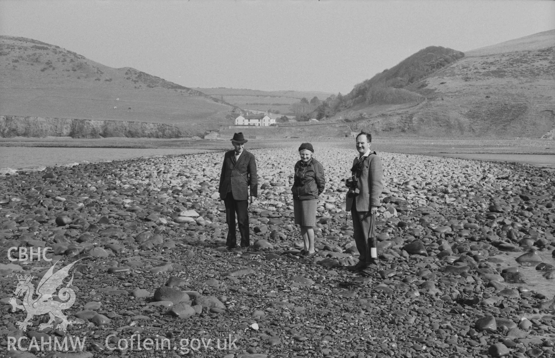 Digital copy of a black and white negative showing view to Wallog house from the extreme tip of Sarn Cynfelyn at lowest ebb of 29ft 7inch tide; 15:45-15:55hrs. Three people posing for camera in foreground. Photographed by Arthur Chater on 4 April 1969. Looking east from Grid Reference c. SN 584 858.