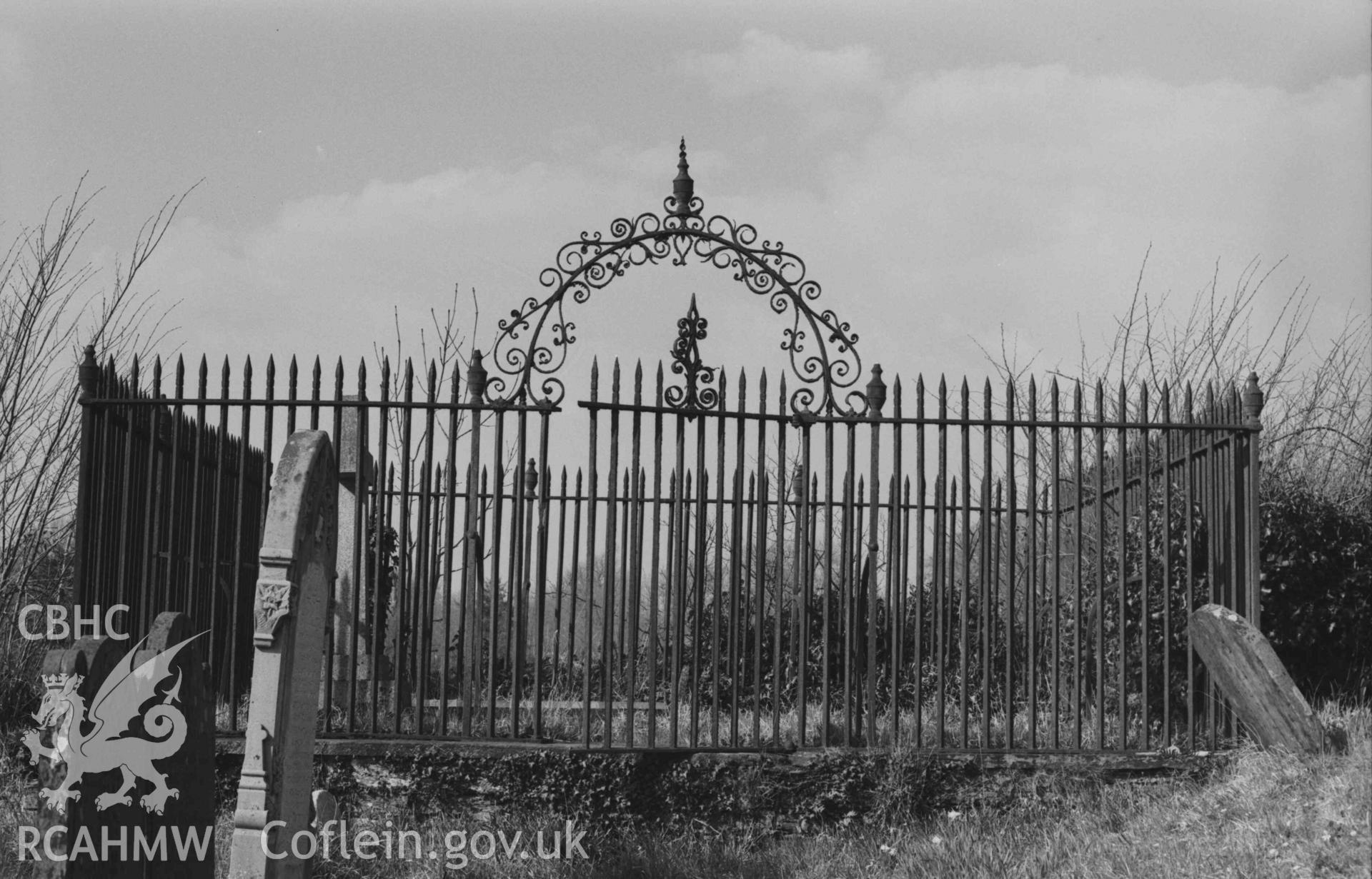 Digital copy of a black and white negative showing wrought iron grace enclosure at the north west corner of St Cynllo's churchyard, containing the graves of Lt.-Col Herbert Rhys, d. 1932; J.O.D. 1850; a stone of 1837; Rhys Jones Lloyd, b. 1827, d. 1889. Photographed by Arthur Chater on 7 April 1969. Looking north from Grid Reference SN 1993 4580.