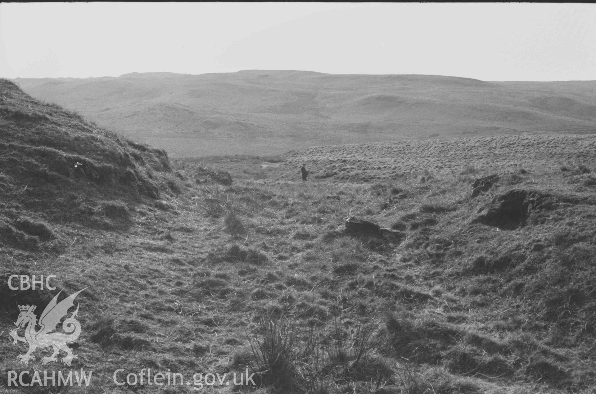 Digital copy of a black and white negative showing the old road in a slight rock-cutting at its highest point on Esgair Hengae. Photographed by Arthur Chater on 8 April 1969. Looking west from Grid Reference SN 8110 6761.
