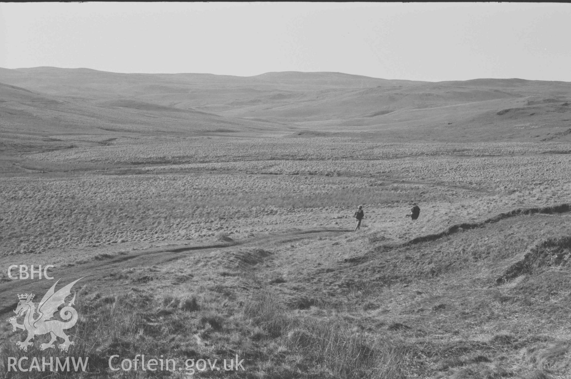 Digital copy of a black and white negative showing the old road joining the new road (left) to Claerwen; looking up the Afon Claerddu to Trawssallt. Photographed by Arthur Chater on 8 April 1969. Looking north west from Grid Reference SN 8085 6760.