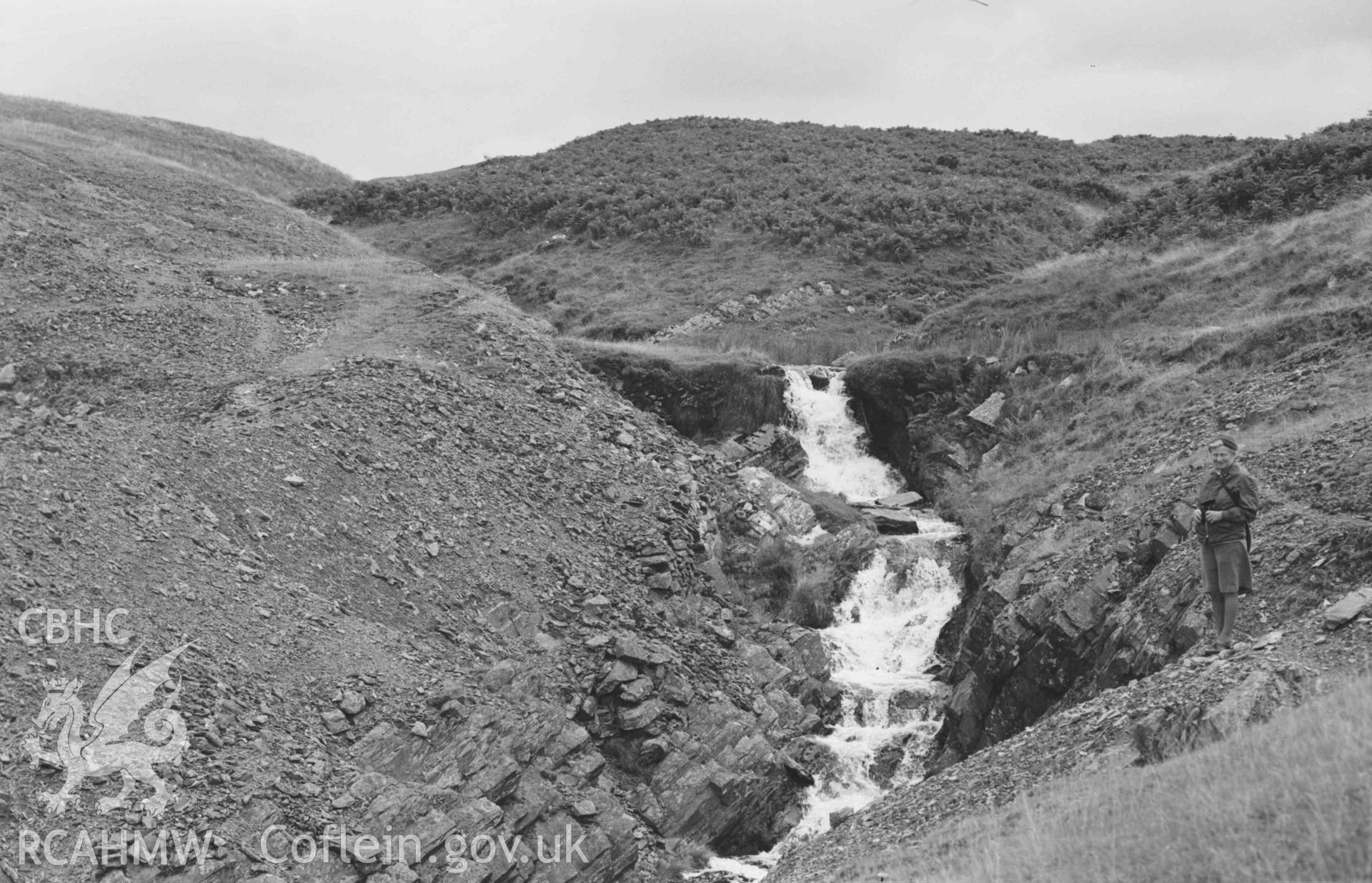 Digital copy of a black and white negative showing waterfall on the Nant Rhysgog and Rhysgog lead mine spoil heap. Photographed by Arthur Chater on 23 August 1969. Looking south south east from Grid Reference SN 6807 5380.