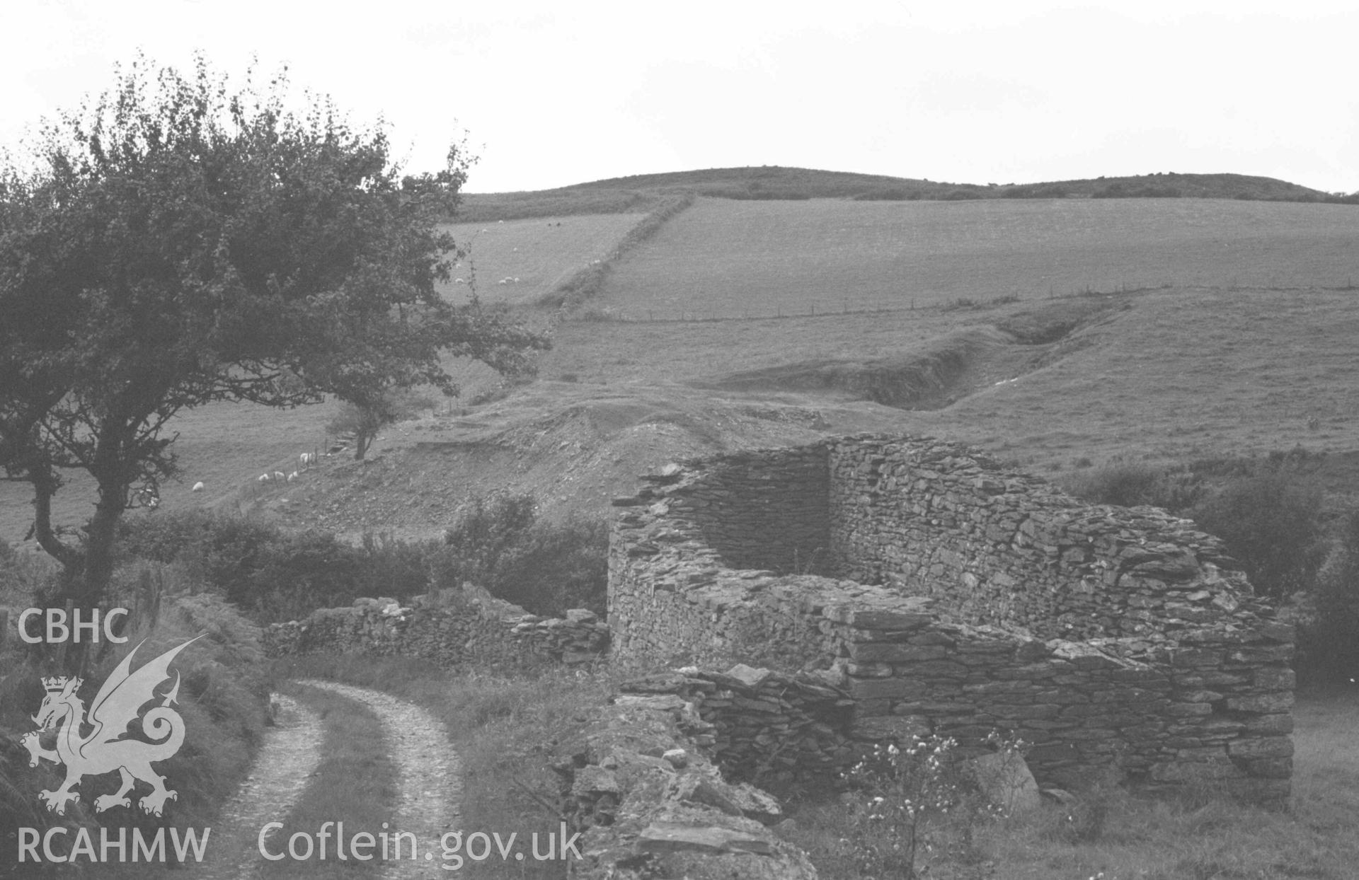 Digital copy of a black and white negative showing view 200m north west of Capel Soar; old mine shaft in field in the middle distance; very narrow, thick-walled ruin (possible wheelpit) in foreground. Photographed by Arthur Chater on 27 August 1969, looking west from Grid Reference SN 6688 9120.