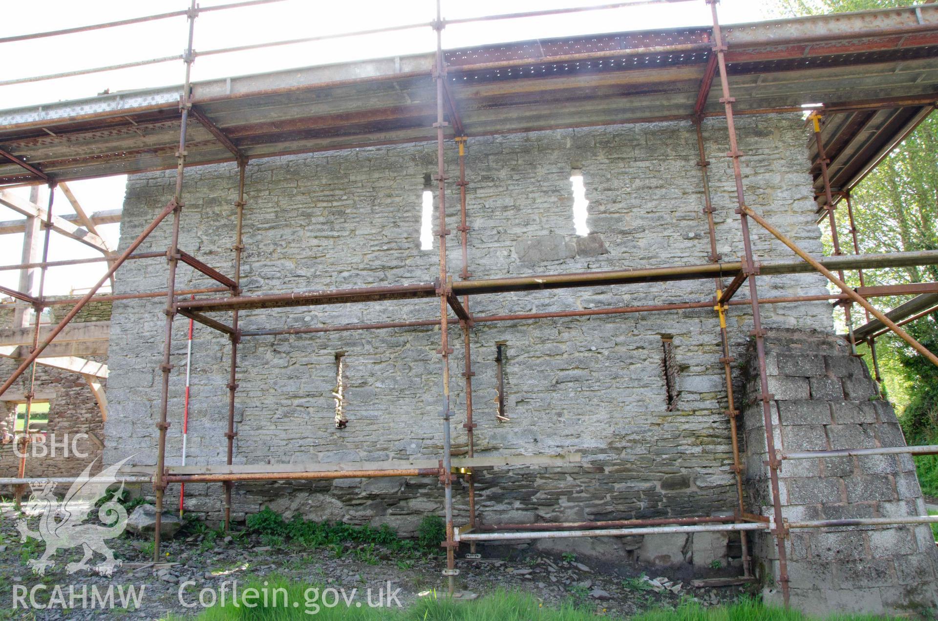 Photograph showing External west elevation of south end of barn. The five ‘arrowslit’ windows were in the gable end of the earlier barn. The west wall of the later barn continues to the left of the ranging pole. From a Photographic Survey of outbuildings at Upper House Farm Evenjobb, submitted as part of Listed Building consent. Photograph taken by Christopher Welch in April/June 2024.
