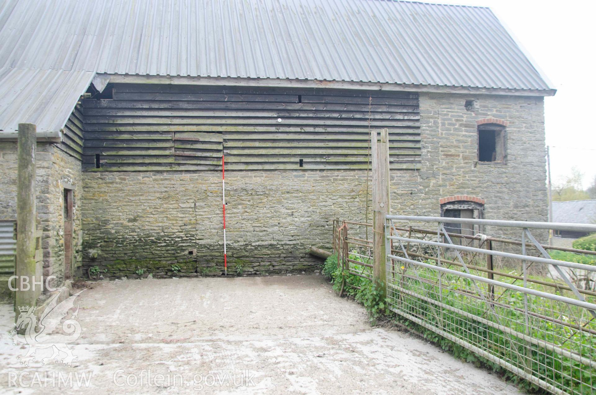 Photograph showing North elevation of cowhouse. Note dairy added at w end (straight joint alongside brick arch), and note earlier straight joint to left of ranging pole. From a Photographic Survey of outbuildings at Upper House Farm Evenjobb, submitted as part of Listed Building consent. Photograph taken by Christopher Welch in April/June 2024.