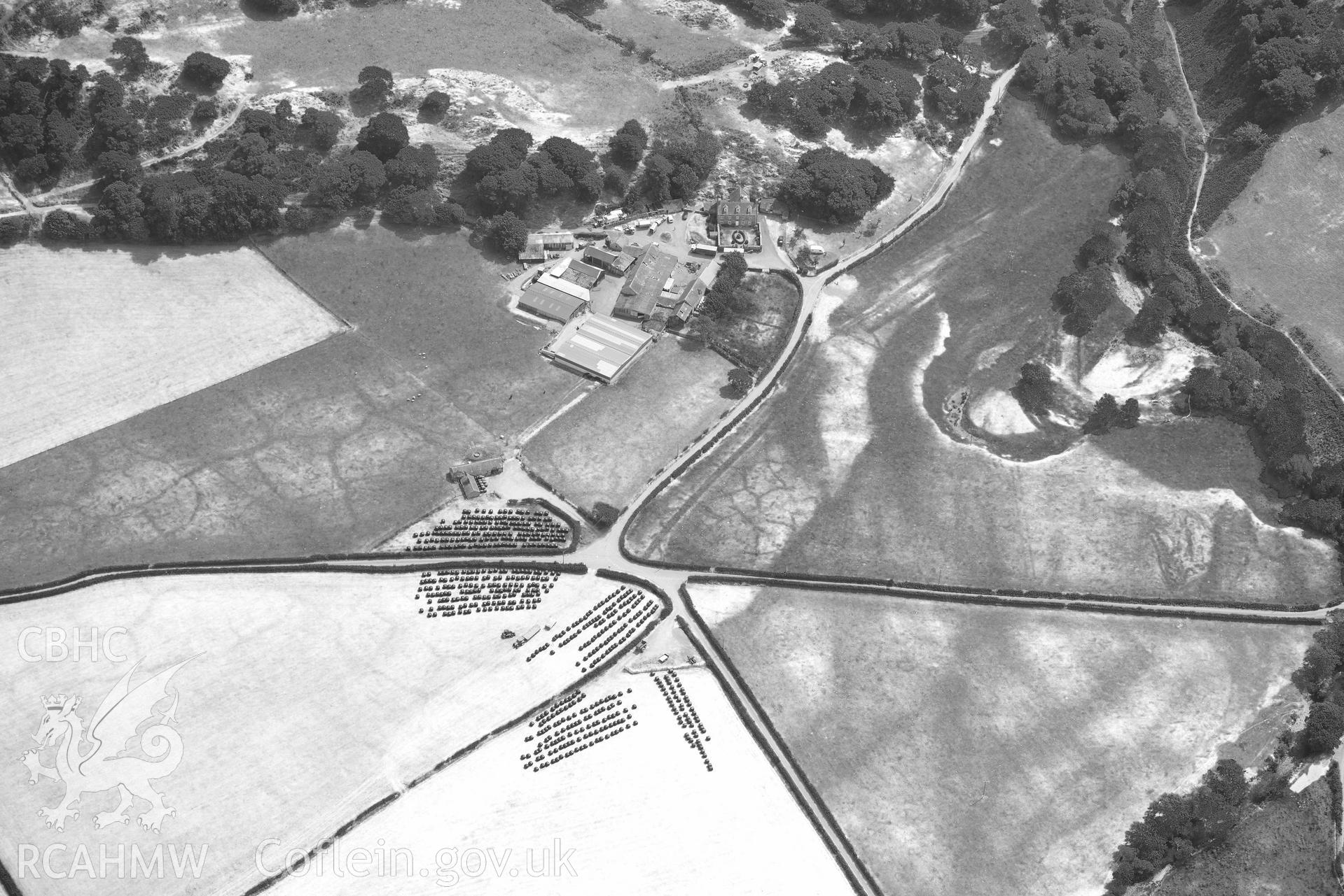 Caer Berllan farm and ditch, with silage bales. Oblique black and white aerial photograph taken during the Royal Commission’s programme of archaeological aerial reconnaissance by Toby Driver on 10 July 2018.