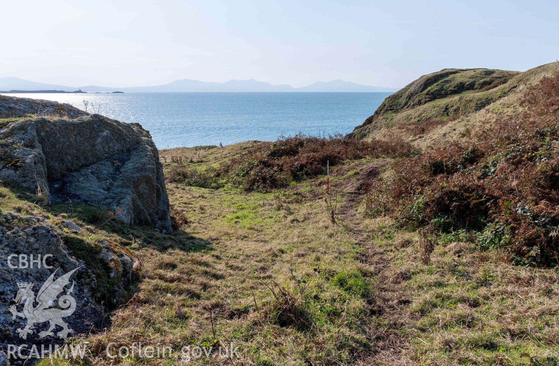 Twyn y Parc Coastal Promontory Fort. View southeast of rock outcrop and outer ditch to the south of the outer gateway running to Porth Ceri-cochion (with scale).