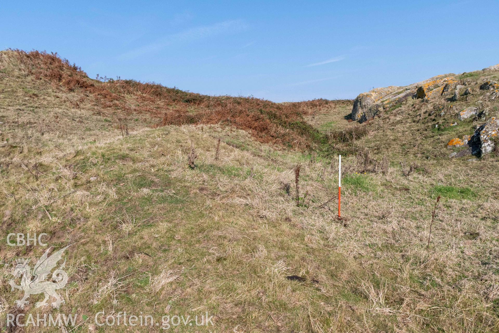 Twyn y Parc Coastal Promontory Fort. View northwest of rock outcrop and outer ditch running to the outer gateway from Porth Ceri-cochion (with scale). The towering inner rampart can be seen to the left.