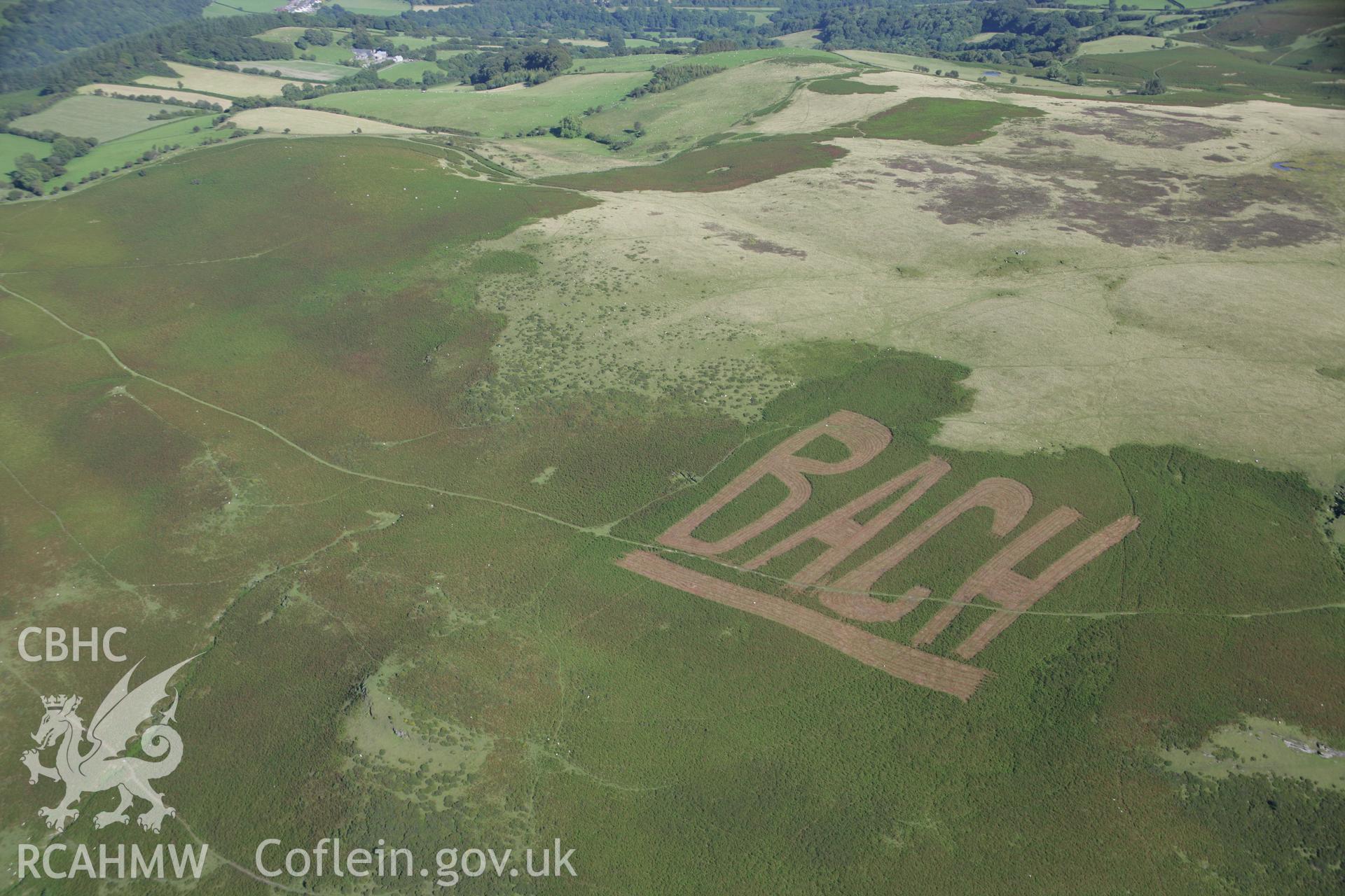 RCAHMW colour oblique aerial photograph of hillside protest graffiti by BACH (Builth Against Closing Hospitals), at Builth Wells. Taken on 08 August 2007 by Toby Driver