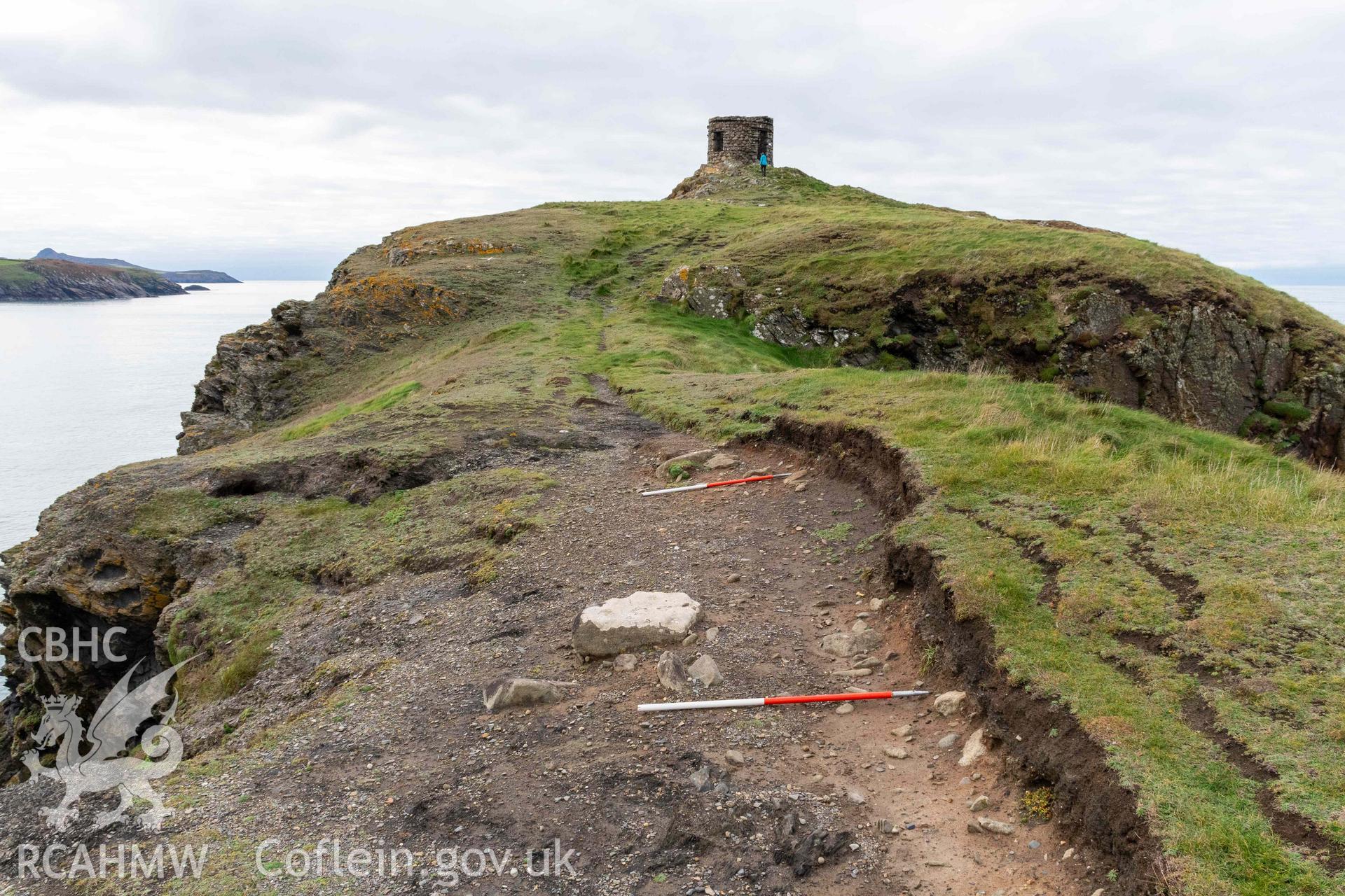 Trwyn Castell coastal promontory fort. View looking west across the narrowest point of the promontory where erosion has exposed walling of the forts defences (with scale).