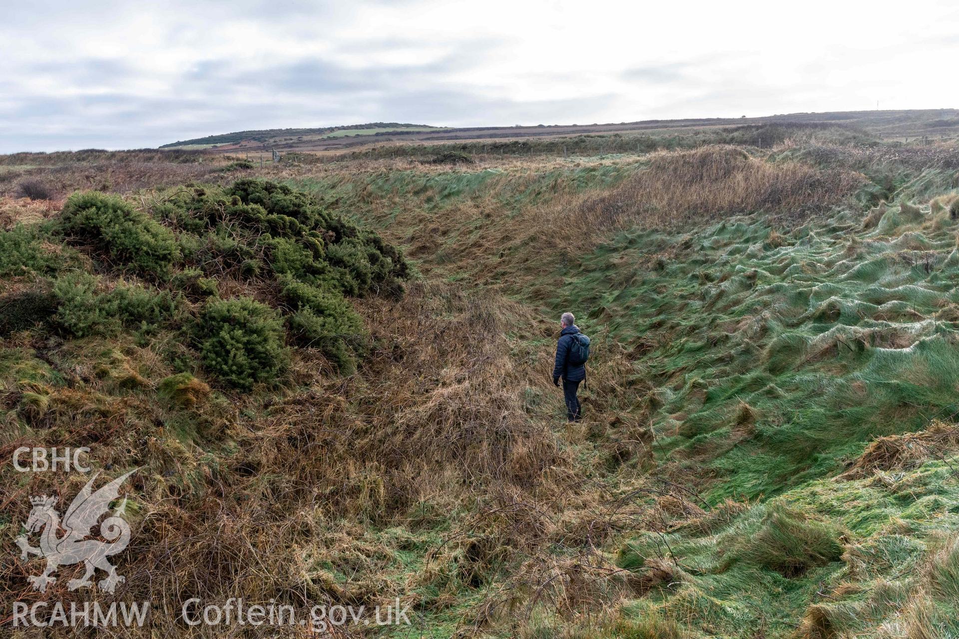 Caer Aber Pwll coastal promontory fort. Looking east along the ditch between the outer and middle defensive banks on the south side of the fort (with human scale).