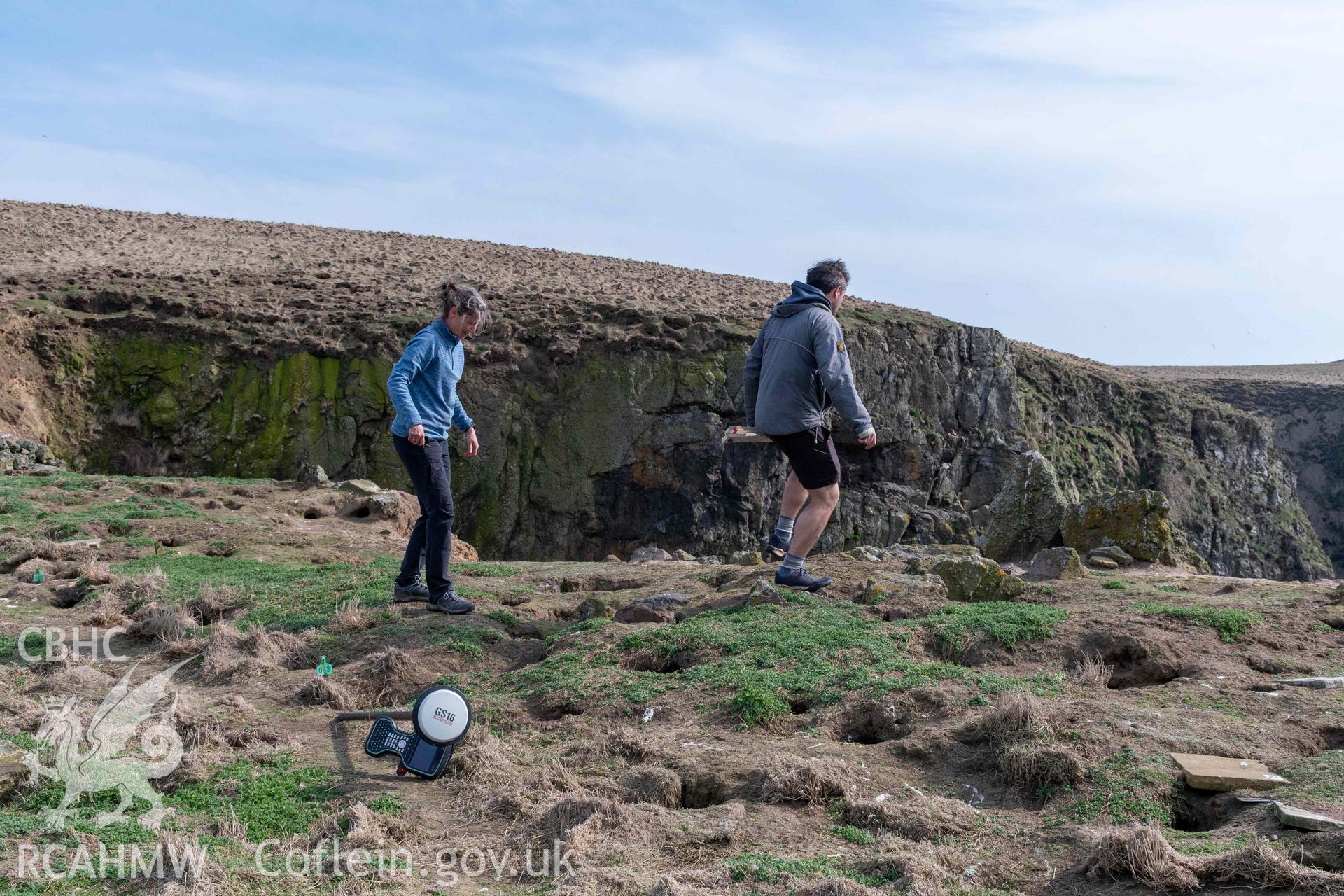 RCAHMW investigator and Skomer warden walking carefully across to the southwest corner of the building to avoid damage to the puffin burrows.
