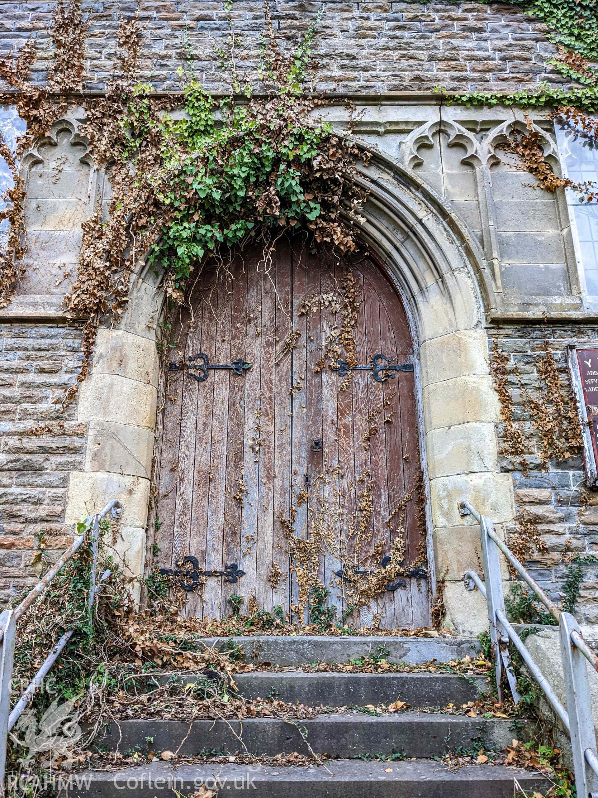 Main arched entrance doorway. Vegetation overgrowing